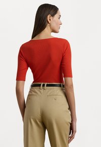 Κόκκινη ριπ μπλούζα με bateau λαιμόκοψη και κοντά μανίκια, σε συνδυασμό με ψηλόμεσες μπεζ παντελόνες με πίσω τσέπες και μαύρη ζώνη.