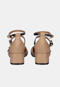 Sandalias de tacón de cuero beige con correas negras y detalles en dorado, con un tacón cuadrado y diseño de correa en el tobillo trasera.