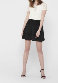 White lace top with short sleeves, structured bodice, and a black layered skirt. The skirt features a smocked waist and smooth texture.