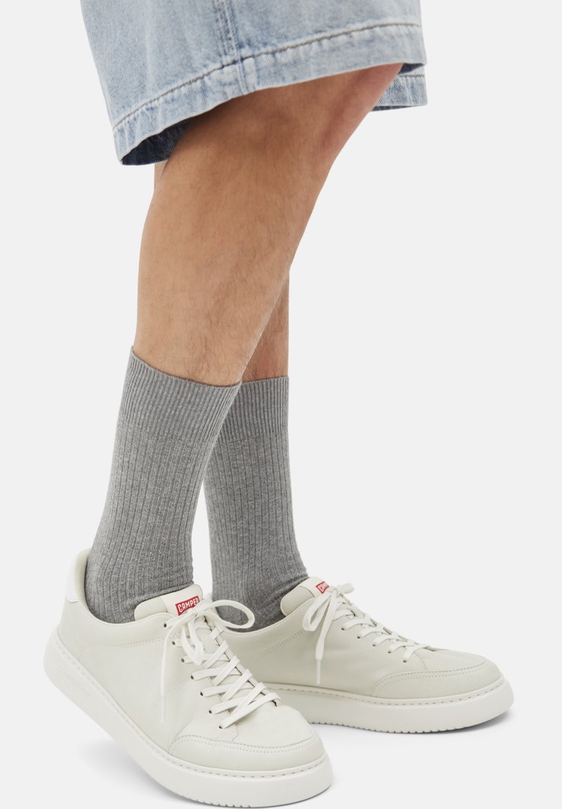 Weiße Sneaker aus Leder mit strukturiertem Obermaterial, weichen Schnürsenkeln und rotem Branding. Graue gerippte Socken. Denim-Shorts mit ausgefranstem Saum.