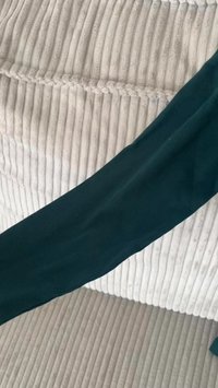 Um tecido ribado verde escuro drapeja sobre uma superfície texturizada cinza claro com linhas verticais pronunciadas, exibindo um material suave e um brilho subtil.