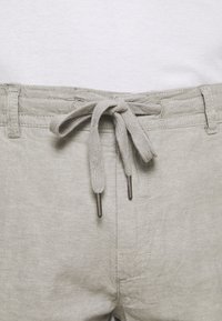 Light grey linen shorts featuring a drawstring waist with fabric ties and metal aglets. Smooth texture and simple stitched accents.