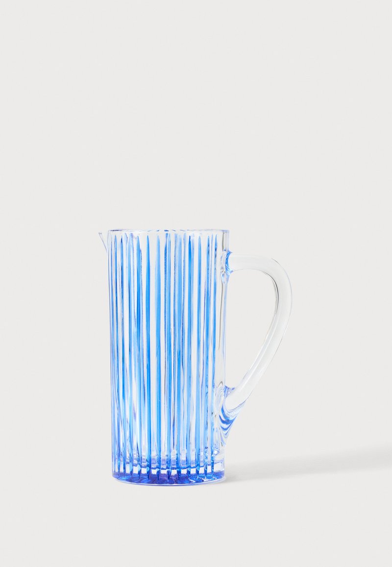 Grand pichet en verre transparent avec des rayures bleues verticales et une anse courbée sur un fond clair uni.