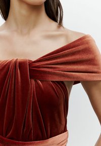Red velvet dress with wide off-the-shoulder straps, gathered texture at the bodice, and a smooth, flowing silhouette.