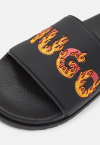Svart slide-sandal med en texturerad sula och ett brett rem med röd och orange flambroderi. Hållbart syntetmaterial.