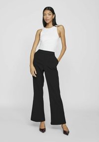 Črne široke hlače z visokim pasom, v kombinaciji z belo brezrokavno majico. Gladek material, minimalističen dizajn, sprednji žepi.
