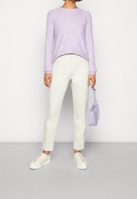 Lilanvärinen neulepaita, kermaiset farkut ja valkoiset alustossut. Pieni, teksturoitu lilakäsilaukku olkahihnalla. Rentoa asua.