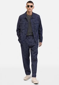 Navy patterned jacket and pants set in lightweight fabric, featuring floral designs. Paired with a dark shirt and beige shoes.