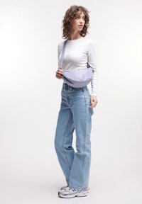 Vaalean liila olkalaukku, joka on valmistettu kankaasta, kaarevalla muotoilulla ja säädettävällä hihnalla. Yhdistetty valkoiseen pitkähihaiseen paitaan ja sinisiin farkkuihin.