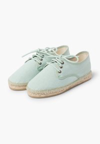 Scarpe in tela verde chiaro con design stringato, punta tonda e suole avvolte in juta. Presentano occhielli in metallo e dettagli cuciti.