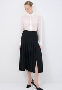 Camicia bianca trasparente con colletto, abbinata a una gonna plissettata nera con bottoni laterali e uno spacco alto fino alla coscia. Scarpe con tacco nere.
