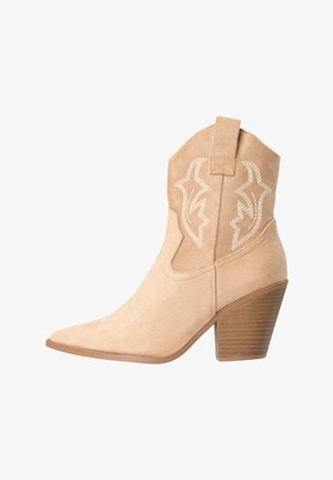Bota vaquera de ante beige hasta media pantorrilla con tacón bloque apilado y patrones decorativos bordados en blanco en la parte superior del tubo.