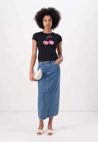 T-shirt nera a maniche corte con grafica di ciliegie glitterate, abbinata a una gonna maxi in denim blu, borsa bianca e sandali bianchi open-toe.