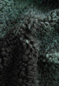Tessuto testurizzato in tonalità di verde scuro e nero, caratterizzato da una superficie fuzzy e morbida con vari spessori e anelli. Aspetto morbido e spesso.
