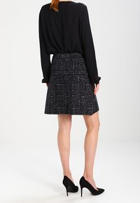 Zwarte blouse met lange mouwen, gecombineerd met een gestructureerde rok van grijs en zwart tweed. G gedragen met zwarte hoge hakken.