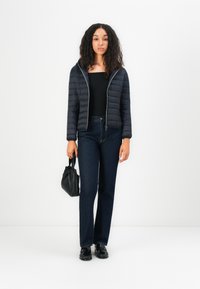 Navy pufferjack met rits en doorgestikt textuur, zwarte top, donkere denim flared jeans en zwarte handtas. Glanzende schoenen maken de outfit compleet.