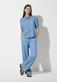 Hellblaues Denimhemd mit Puffärmeln und Knöpfen an der Vorderseite, kombiniert mit lässigen, weiten Jeans in passender Farbe. Modell trägt schwarze und beige Sandalen.