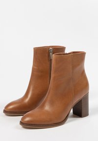 Une paire de bottes en cuir beige à la cheville avec des fermetures éclairs sur les côtés et des talons blocs empilés, sur fond blanc.