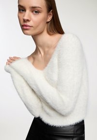 Maglione bianco fluffy a maniche lunghe con scollo ampio, caratterizzato da una texture morbida e spalle scese, abbinato a una gonna nera aderente.