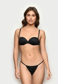 Czarny, wyściełany biustonosz o gładkiej tkaninie i regulowanych ramiączkach. Pasujące czarne stringi z frędzlami z przodu, tworzące teksturowany wygląd.