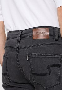 Czarne jeansy z denimu z brązową skórzaną naszywką z logo z tyłu. Oferują tylne kieszenie z zakrzywionym przeszyciem oraz małą metkę marki.