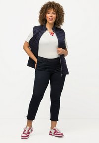 Mörkblå quiltad väst över en ljusgrå t-shirt, matchad med mörka jeans och rosa-randiga sneakers, med en enkel design och eleganta detaljer.