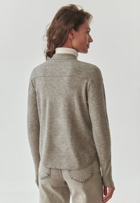 Grauer Pullover mit einem Stehkragen-Design und geripptem Kragen, im lässigen Schnitt mit langen Ärmeln, kombiniert mit hellgrauen Jeans.