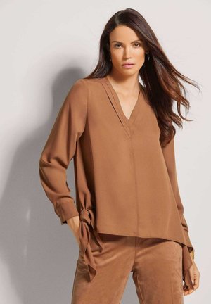 Braune Bluse mit langen Ärmeln, V-Ausschnitt und Bindebändern an der Taille. Glattes, leichtes Material mit dezenten Faltendetails.