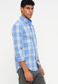 Ανοιχτό μπλε καρό πουκάμισο με λευκές και σκούρες μπλε γραμμές, με χρώμα πουκαμίσου και μακριά μανίκια σηκωμένα, κατασκευασμένο από μαλακό ύφασμα.