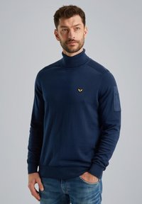 Navyblaue Rollkragensweater aus weichem Stoff. Verfügt über gerippte Bündchen und ein kleines goldenes Logo auf der Brust. Schlichtes, tailliertes Design.