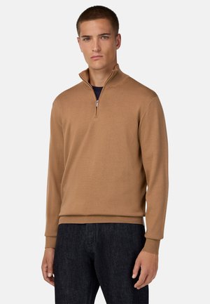 Beiger Halb-Zip-Pullover aus Strickstoff, mit langen Ärmeln und ribbelten Bündchen, kombiniert mit dunkelblauen Jeans.