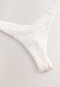 Biele bikini nohavičky s textúrovaným povrchom, trojuholníkovým tvarom a elastickým materiálom so zhrnutými okrajmi.