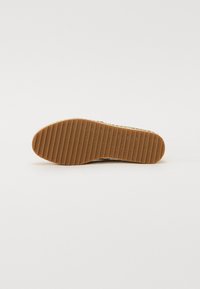 Suela de zapato de goma en marrón claro con estrías verticales y texto de marca en relieve. Bordes lisos y un diseño plano y ancho para mayor estabilidad.