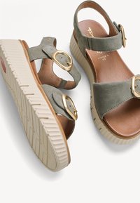 Paire de sandales en daim vert avec des semelles en caoutchouc beige épaisses et des brides avec boucle dorée, conçues pour un confort large.