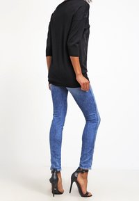 Maglione nero oversize con maniche a tre quarti, abbinato a jeans slim-fit blu e scarpe nere con tacco alto.