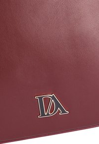 Bolso de cuero burdeos con un logo DA en oro y negro. Textura suave con forma rectangular, diseño minimalista, sin adornos adicionales.