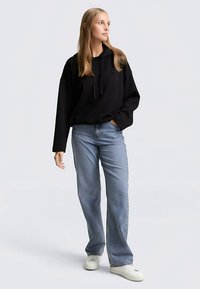 Zwarte hoodie met een losse pasvorm, gecombineerd met lichtblauwe jeans met rechte pijpen en witte sneakers. Simpel ontwerp, geen zichtbare patronen.