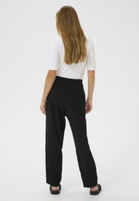 Pantalons larges noirs à taille haute, associés à un haut blanc ajusté. Dotés de poches arrière et d'une finition texturée lisse.