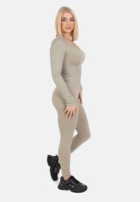 Beige ribbel bodysuit met lange mouwen, aansluitend ontwerp, gecombineerd met zwarte chunky sneakers. Zachte textuur en subtiele contourdetails.