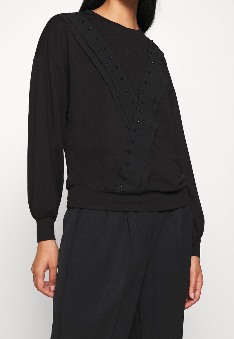 Sweat-shirt noir à manches longues avec un volant texturé et des détails perlés en motif diagonal, doté d'une taille ajustée.