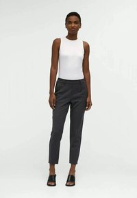 Top branco sem mangas combinado com calças cinza-escuras de corte justo. Design slim fit, textura suave e estilo minimalista. Sandálias slides pretas.