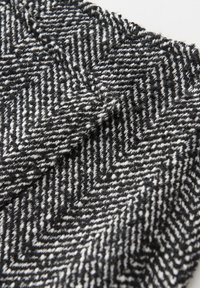 Gros plan d'un tissu en laine à motif chevrons noir et blanc avec une apparence tissée et texturée.