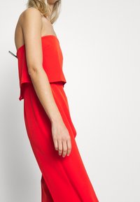 Combinaison rouge bustier avec un haut ample et raccourci et des jambes larges et fluides. Tissu lisse, détails minimalistes, adaptée à diverses occasions.
