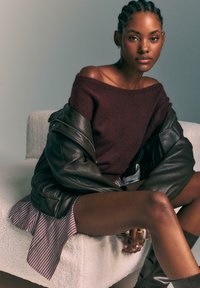 Bordo off-shoulder pulover v kombinaciji s temno usnjeno jakno, stripe krilo in rjave škornje do kolen. Gladka tekstura.