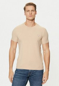 T-shirt beige a maniche corte con collo rotondo e piccolo logo a triangolo rosso sul petto. Realizzata in cotone morbido, stile slim fit.