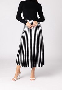 Haut noir à manches longues côtelé associé à une jupe midi rayée noire et blanche. La jupe présente des rayures verticales et une silhouette évasée.