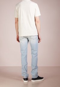 En enkel vit T-shirt, kortärmad, avslappnad passform, i kombination med ljusblå jeans, raka ben, och svarta sneakers med vita sulor.