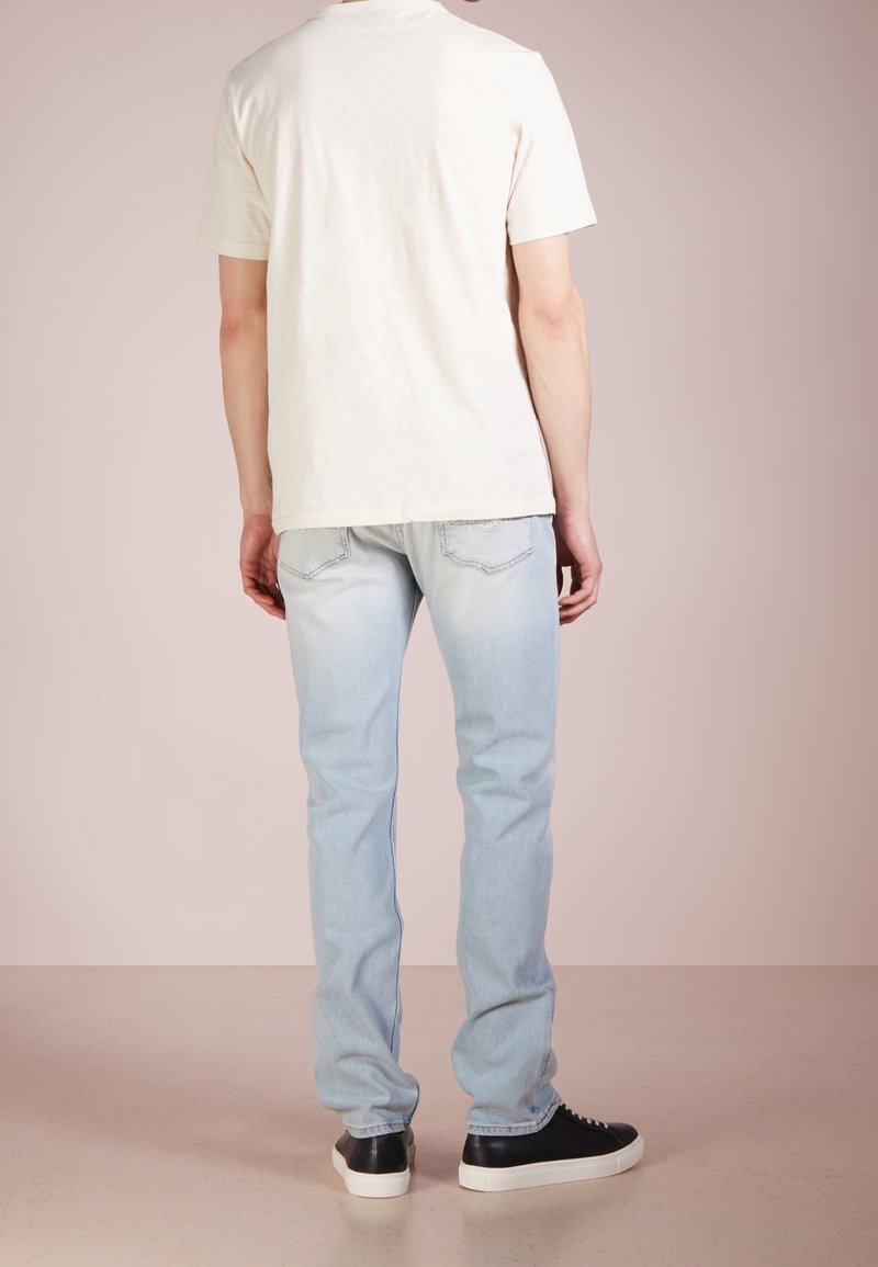 En enkel vit T-shirt, kortärmad, avslappnad passform, i kombination med ljusblå jeans, raka ben, och svarta sneakers med vita sulor.