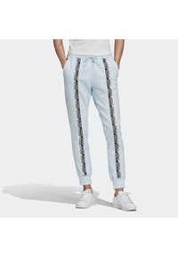 Ljusblå sweatpants med svarta sidosträck som har upprepad text. Elastisk midja med dragsko och smalnande öppningar vid anklarna. Vita skor.