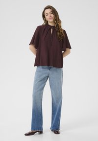 Bordeaux plissés blouse met korte mouwen, sleutelgat en strikdetail, gecombineerd met lichtblauwe denim wijde pijpen jeans en donkere hakken schoenen.